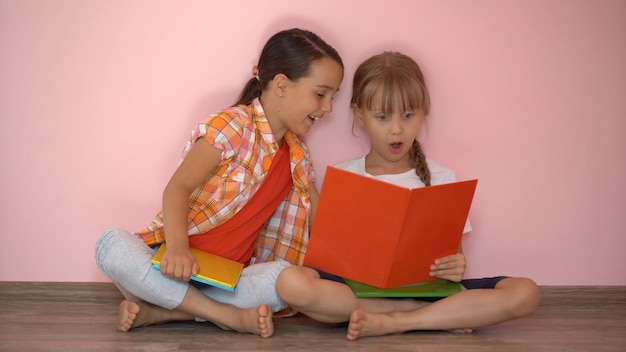 Niñas encantadoras están leyendo un libro. El concepto de educación. aislado sobre fondo rosa