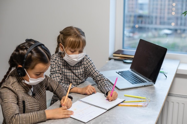 Niñas de la escuela primaria jóvenes con máscara protectora facial viendo la clase de educación en línea. Concepto de educación de bloqueo de coronavirus o Covid-19.