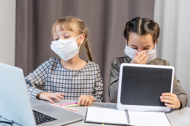 Niñas de la escuela primaria jóvenes con máscara protectora facial viendo la clase de educación en línea. Concepto de educación de bloqueo de coronavirus o Covid-19.