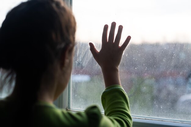 Las niñas están paradas en la oscuridad, mirando por la ventana, tristes