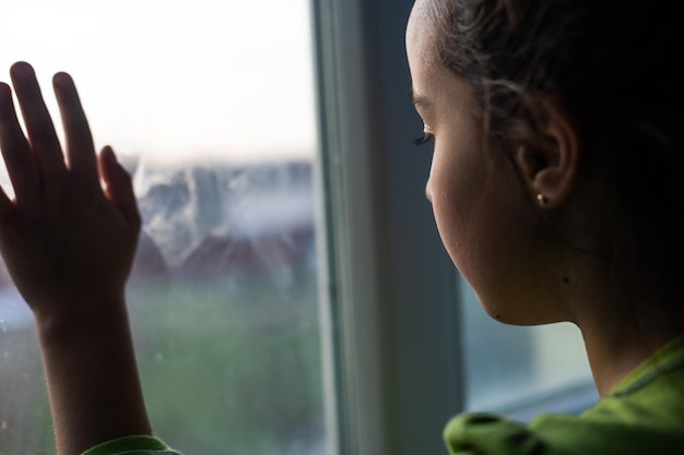 Las niñas están paradas en la oscuridad, mirando por la ventana, tristes