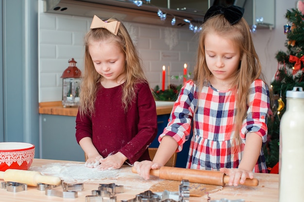 Niñas felices adorables que hornean galletas de jengibre de Navidad en la víspera de Navidad