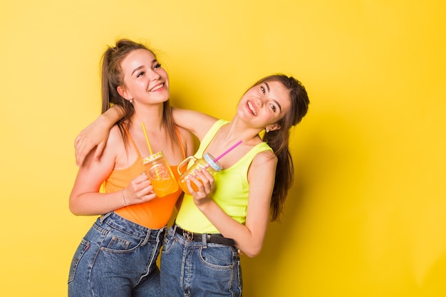 Foto niñas felices sonriendo con bebidas sobre fondo amarillo