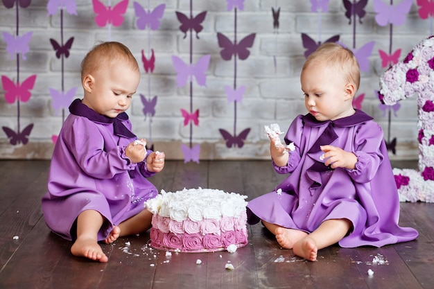 Niñas gemelas de un año que seleccionan su primer cumpleaños y comen un pastel.