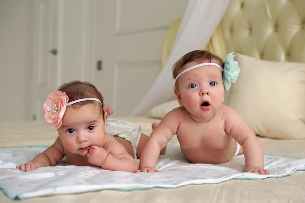 Las niñas gemelas en pañales se acuestan en la cama en su estómago