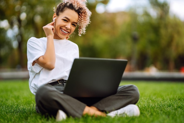 Las niñas hablan en una videollamada con colegas en una sesión informativa en línea en una computadora portátil moderna sentada en el parque