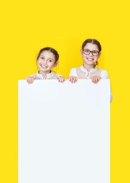 Niñas hermanas sosteniendo un cartel vacío blanco y sonriendo Niñas sosteniendo un tablero de anuncios blanco