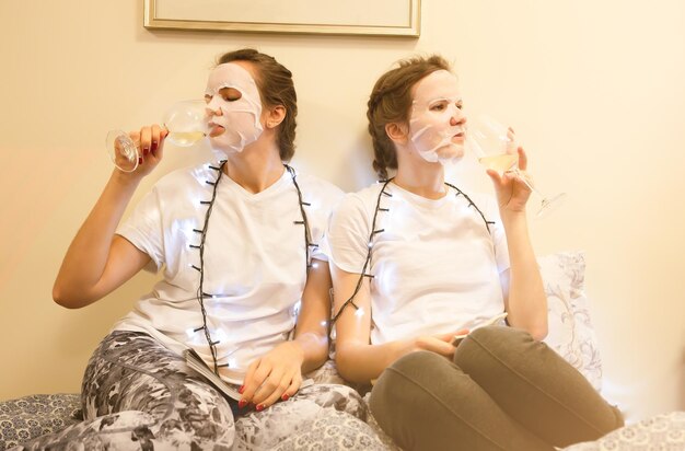 Niñas en hoja de máscara de piel en la cara Procedimientos de belleza en casa Despedida de soltera Revista de lectura de mujeres