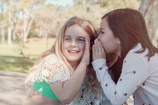 Niñas jóvenes de etnia mixta jugando niños susurrando chinos en el parque, mejores amigos y amistad positiva, concepto de mejores amigos para siempre