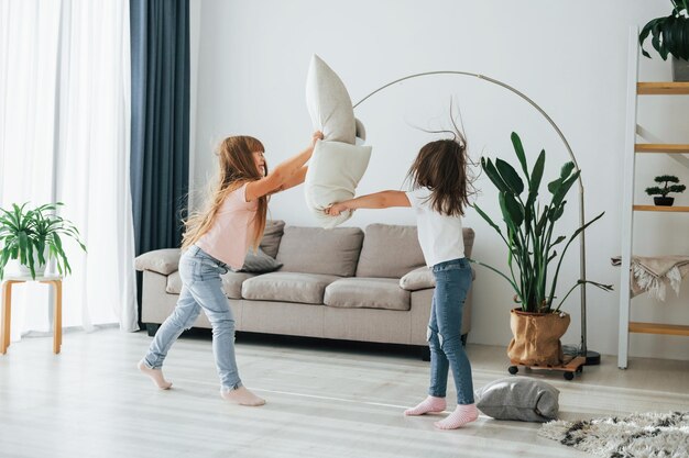 Las niñas juegan al juego de pelea de almohadas Los niños se divierten juntos en la sala doméstica durante el día