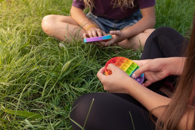 Las niñas juegan al juguete popular pop-it con toque de silicona colorido al aire libre en la hierba verde