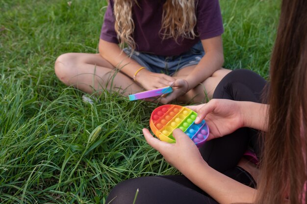 Las niñas juegan al juguete popular pop-it con toque de silicona colorido al aire libre en la hierba verde