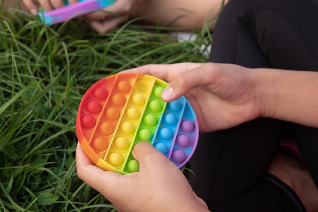 Las niñas juegan el juguete popit popular colorido del tacto del silicón al aire libre en la hierba verde