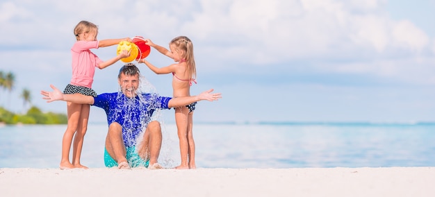 Niñas lindas divirtiéndose con papá en la playa blanca