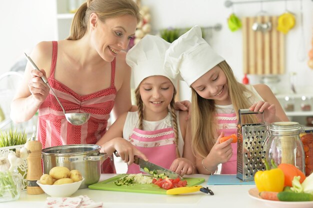 Niñas lindas con su madre preparando una deliciosa ensalada fresca en la cocina