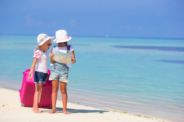 Niñas con maleta grande y mapa en playa tropical