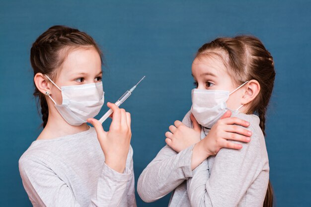 Las niñas con máscaras médicas miran una jeringa con medicamentos en la mano. Vacunación, tratamiento de niños. Prevención de brotes