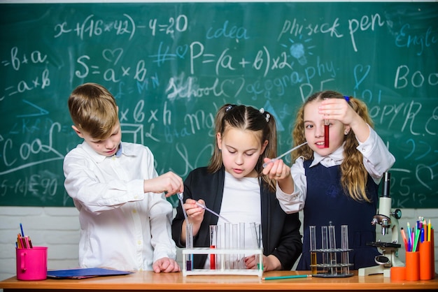 Niñas y niños realizando experimentos con líquidos Tubos de ensayo con sustancias líquidas coloridas Estudio de estados líquidos Alumnos de grupo con tubos de ensayo estudian líquidos químicos Laboratorio escolar