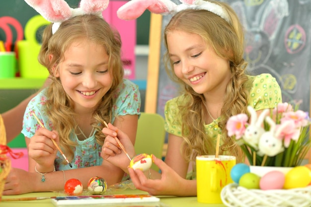 Niñas con orejas de conejo decorando huevos de Pascua en casa