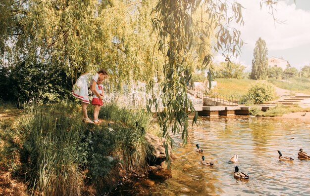 Las niñas a orillas del río alimentan a los patos.