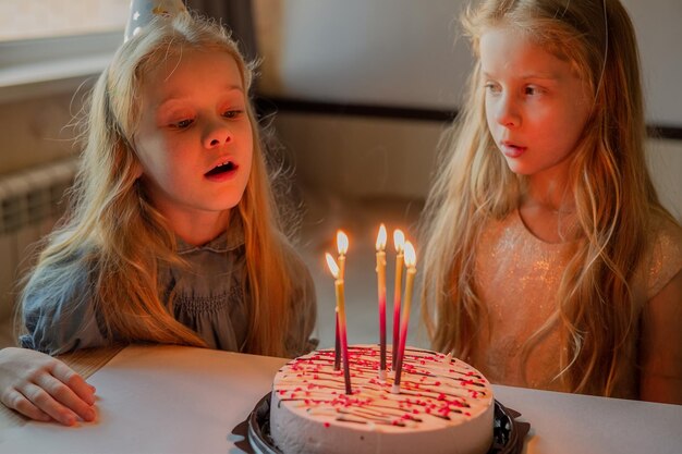 Niñas pequeñas, niños gemelos, soplan velas, pastel, fiesta de cumpleaños en casa, vacaciones durante la cuarentena.