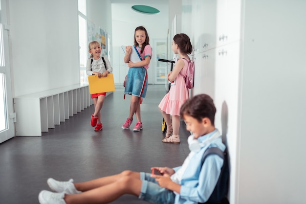 Niñas de pie y mirando al niño sentado en el suelo en la escuela