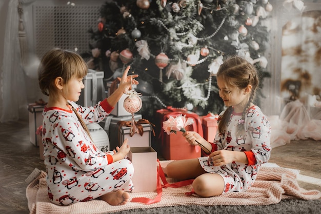 Niñas en pijama abren caja de regalo bajo el árbol de Navidad