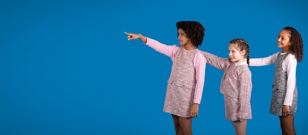 Niñas positivas y diversas en ropa casual se divierten señalando con el dedo el espacio libre