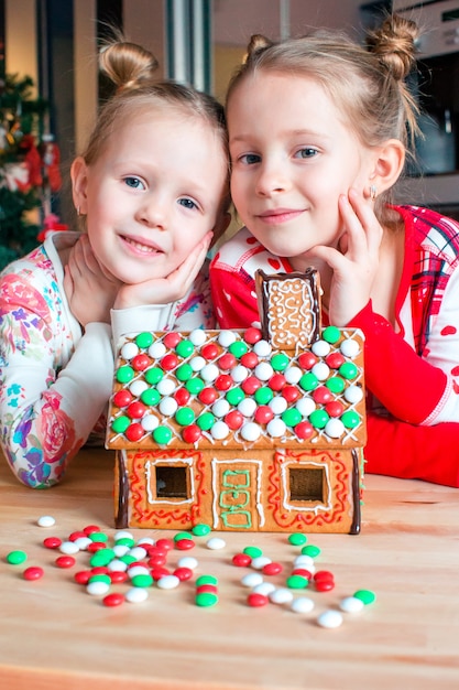 Niñas que hacen la casa de pan de jengibre de la Navidad en la chimenea en sala de estar adornada.