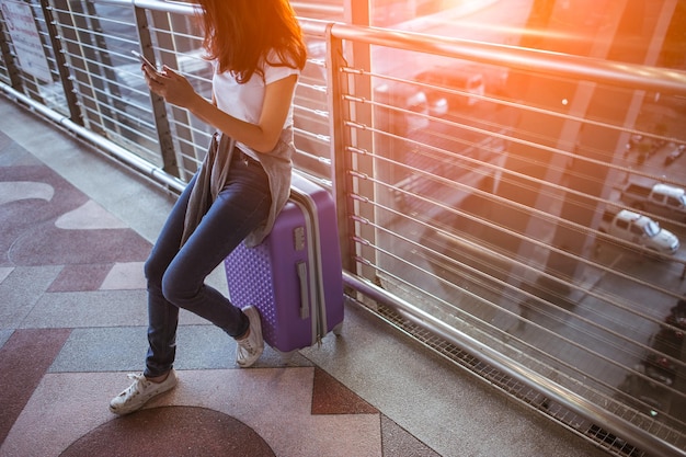 Niñas que usan teléfonos inteligentes para verificar el vuelo o registrarse en línea en el aeropuerto juntas, con equipaje. Viajes aéreos, vacaciones de verano o aplicación de teléfono móvil