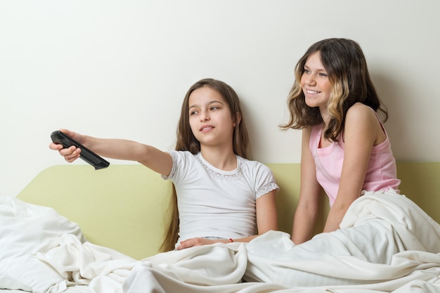 Niñas sentadas en casa en la cama y viendo televisión