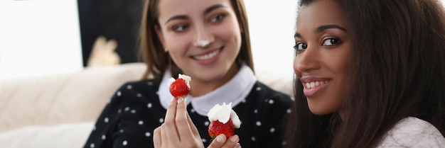 Niñas sonrientes comiendo deliciosas fresas frescas cubiertas con crema batida