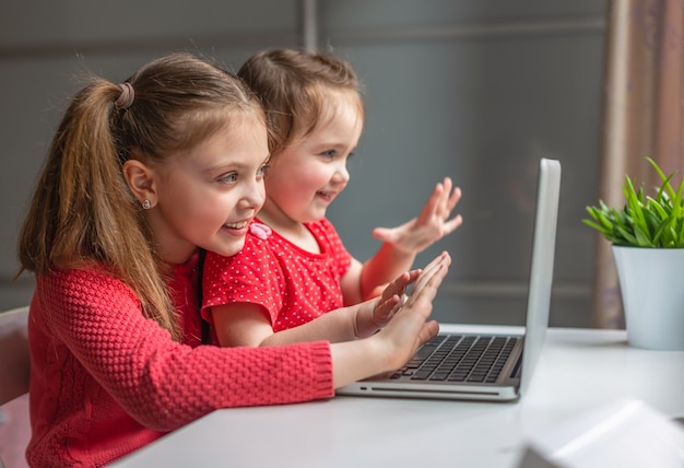 Las niñas sonrientes miran la computadora portátil. Se comunica en línea en casa