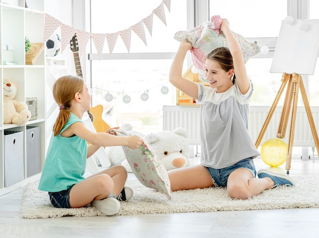 Niñas sonrientes peleando con almohadas en la habitación de los niños