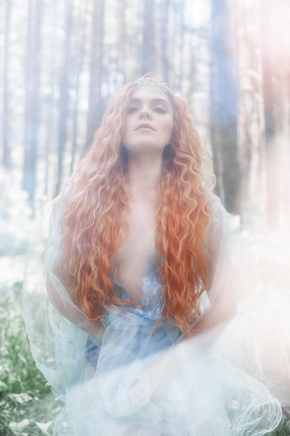 Ninfa del bosque de mujer hermosa pelirroja con un vestido azul claro transparente en el bosque girando en danza. Chicas de pelo rojo. Retrato de moda de arte de cuento de hadas de mujer de hadas en bosque de verano