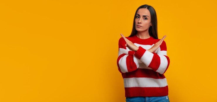 Foto ¡de ninguna manera aquí! mujer joven seria y segura está cruzando las manos y mirando directamente a la cámara sobre fondo amarillo