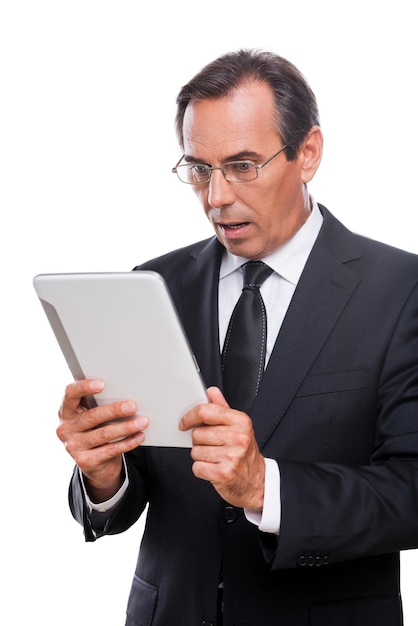 ¡De ninguna manera! Hombre maduro sorprendido en ropa formal sosteniendo tableta digital y manteniendo la boca abierta mientras está de pie aislado sobre fondo blanco.