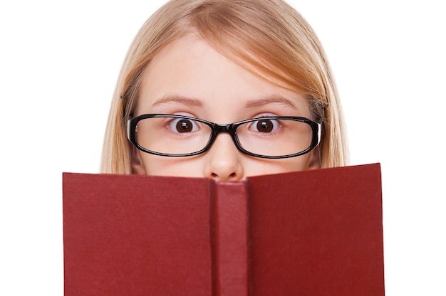 ¡De ninguna manera! Niña sorprendida leyendo el libro y manteniendo la boca abierta mientras está de pie aislado en blanco