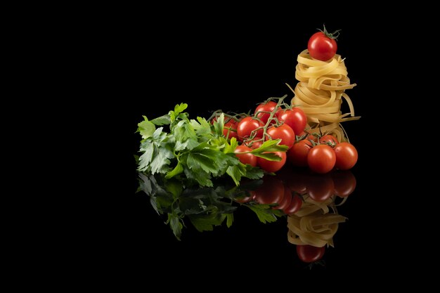 Ninho de macarrão com tomate vermelho isolado no fundo reflexivo preto.