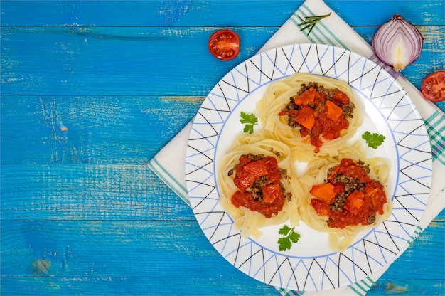 Ninho de macarrão tagliatelle com molho à bolonhesa e legumes em um prato. Vista do topo