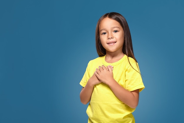 niñita con camiseta amarilla con las manos en el corazón en el fondo azul