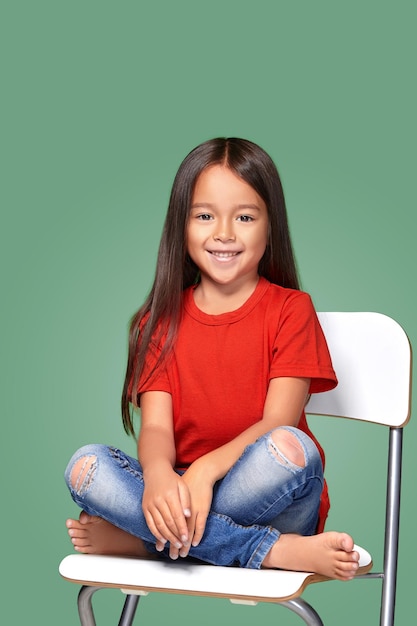 niñita con camiseta roja y posando en una silla con fondo verde