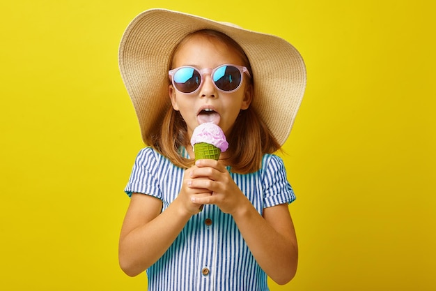 niñita comiendo helado con un fondo amarillo aislado vestida con ropa de verano y gafas de sol