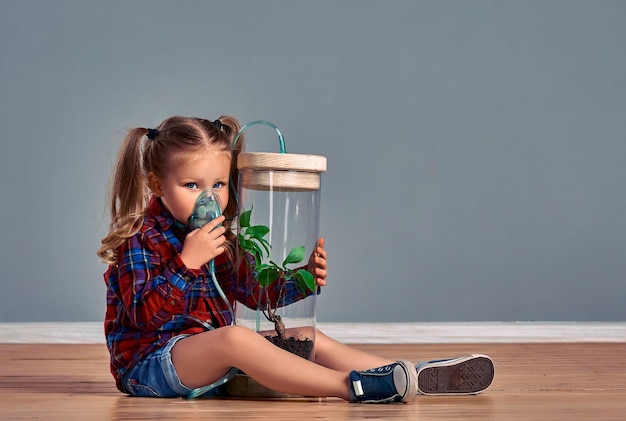 Una niñita linda está respirando a través de una máscara inhalando su oxígeno a través de un espaciador mientras mira con sus ojos cansados El concepto de contaminación del aire y el medio ambiente por la actividad humana Copiar espacio