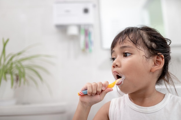 Una niñita linda limpiándose los dientes con un cepillo de dientes en el baño