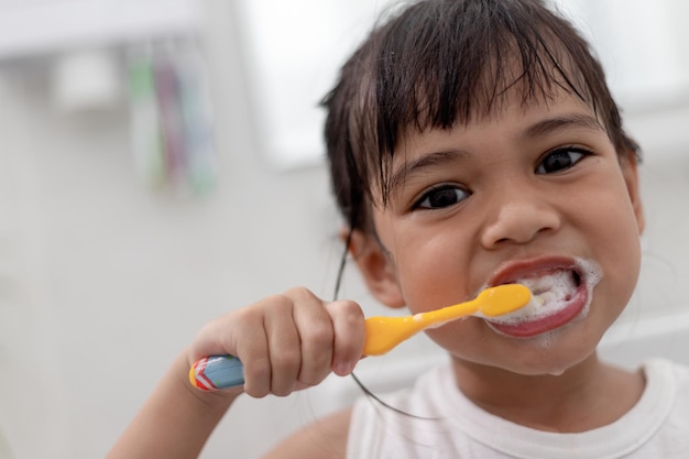 Una niñita linda limpiándose los dientes con un cepillo de dientes en el baño