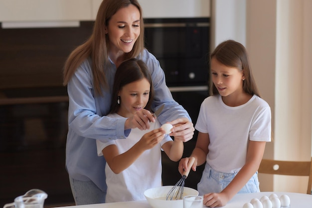 Una niñita linda y su hermosa mamá con delantales juegan y se ríen mientras amasan la masa en la cocina