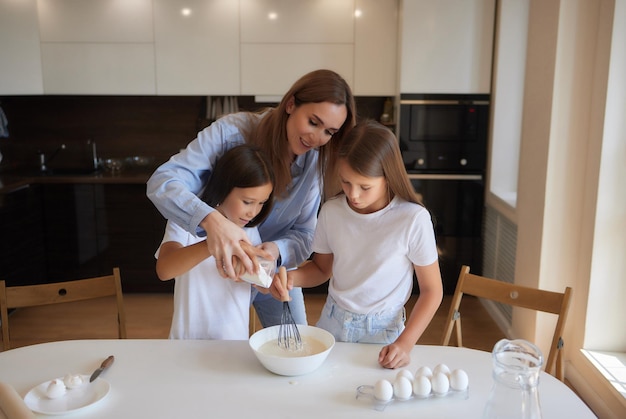 Una niñita linda y su hermosa mamá con delantales juegan y se ríen mientras amasan la masa en la cocina