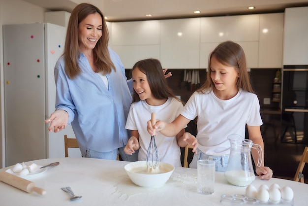 Una niñita linda y su hermosa mamá con delantales juegan y se ríen mientras amasan la masa en la cocina