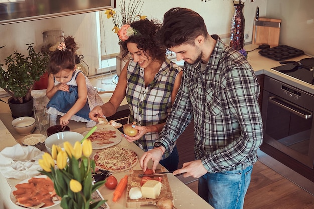 Una niñita linda y sus hermosos padres preparan pizza mientras cocinan en la cocina de casa.